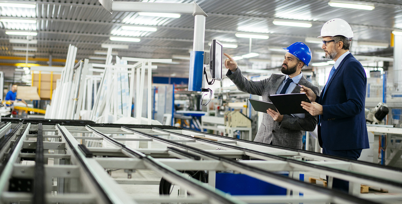 Two men, engineer explaining machine functioning to company CEO. Both wearing hard hats and looking at computer screen.