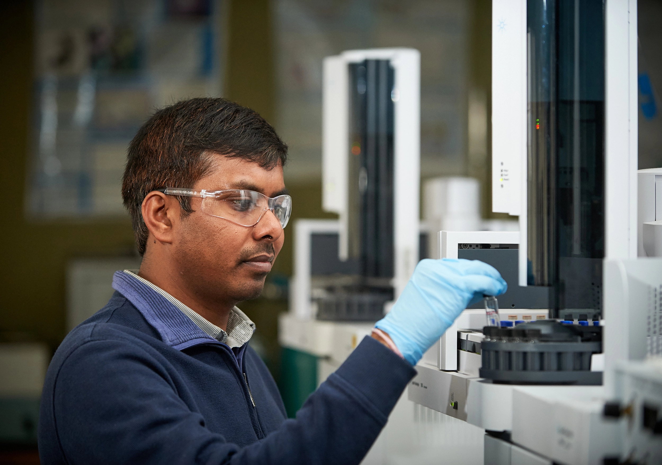 Student wearing glasses and blue glove holding test tube working in the lab.
