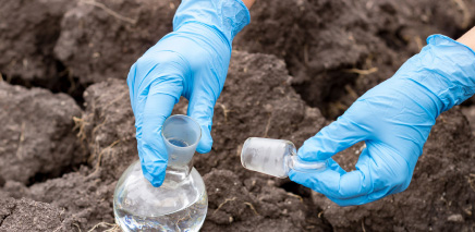 Close up of hands with gloves holding flask and test tube.