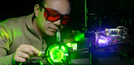 Asian male wearing protective glasses working on neon green machinery.